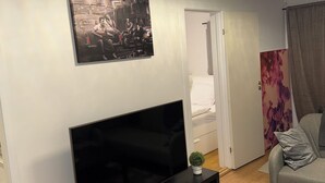 En stue med et fladskærms-tv på et stativ, en lille plante på stativet og et billede over tv'et.
