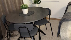 Et rundt spisebord med fire stole, en potteplante og et indrammet kunstværk på væggen.