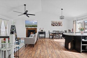 A modern living room with a fireplace, a dining area, and a kitchen island.