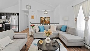 Un salon moderne avec un canapé gris, une table basse agrémentée d’objets décoratifs et une cuisine en arrière-plan.