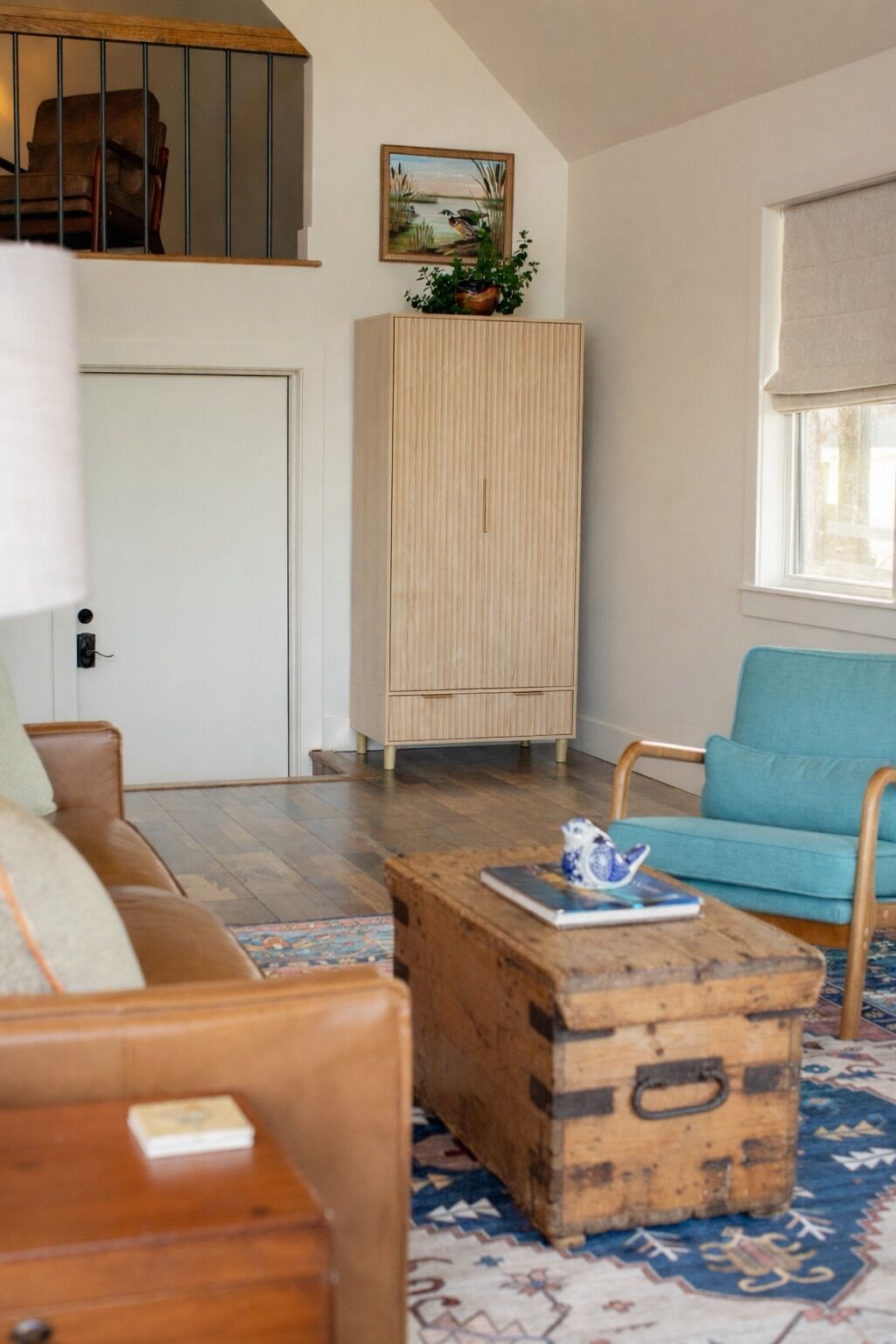 Ein Wohnzimmer mit einem Holzschrank, einem blauen Sessel, einer Holzkiste und einem gemusterten Teppich.