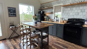 Una cocina con una mesa de madera, taburetes de bar, una estufa negra y un letrero en una pizarra.