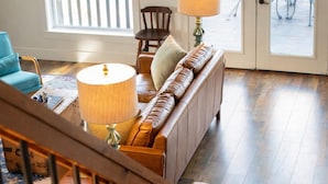 Una escalera conduce a una sala de estar con un sofá, una lámpara y vistas a un patio exterior.