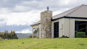 A modern house with a stone chimney, large windows, and a view of the surrounding landscape. - Snowy Mountains Retreat - 10 Mowamba Way (Moonbah)