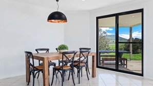 A dining area with a wooden table and black chairs, a hanging pendant light, and a view of a green landscape through a glass door. - Snowy Mountains Retreat - 10 Mowamba Way (Moonbah)