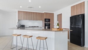 A modern kitchen with a central island, bar stools, a refrigerator, and a microwave. - Snowy Mountains Retreat - 10 Mowamba Way (Moonbah)