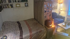 Et hyggeligt soveværelse med seng, bogreol, en billedvæg, lampe og et lille bord med et lys.