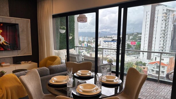 Un comedor con una mesa preparada para cuatro personas, un sofá y un televisor al fondo.