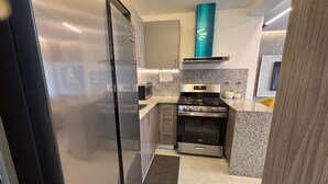 Una cocina compacta con refrigerador, estufa, horno y encimeras de granito.