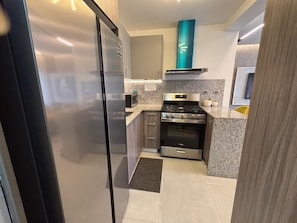 Una cocina compacta con refrigerador, estufa, horno y encimeras de granito.