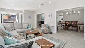 A modern living room with a sectional sofa, a dining area with a wooden table and chairs, and a kitchen in the background. - Sarasota Springs Pool Retreat | Heated Pool • Pet-Friendly • Near Siesta Key (Sarasota)