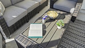 A patio area with wicker furniture, a table with a book, popcorn, and drinks. - Sarasota Springs Pool Retreat | Heated Pool • Pet-Friendly • Near Siesta Key (Sarasota)