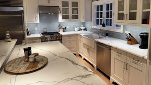 Una cucina moderna con mobili bianchi, un frigorifero in acciaio inossidabile, un fornello a gas e un piano di lavoro in marmo.