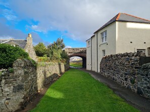 A narrow stone pathway leading to a white building with a stone wall on one side and a stone bridge in the background. - NEW LISTING! Old Police Station, Portsoy - sleeps 4 guests  in 2 bedrooms (BANFF)
