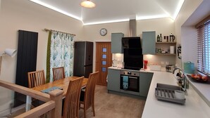 Una cocina moderna con comedor, que incluye una mesa y sillas de madera, horno empotrado y cafetera.