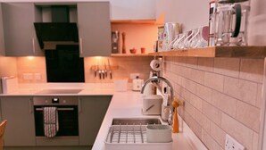 A modern kitchen with a white countertop, a sink, and a coffee machine. - Warm and accessible coastal cottage with sustainable design — coming soon (Lossiemouth)