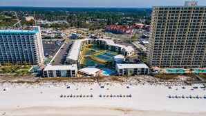 Un resort con playa, canchas de tenis y un edificio grande de varios pisos.