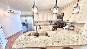 Una cocina con encimera de granito, pileta de acero inoxidable y taburetes de madera.