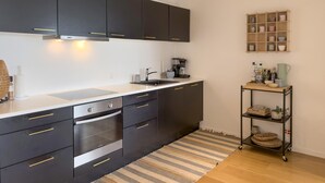 Une cuisine moderne avec des meubles de couleur sombre, un four encastré, une machine à café et une petite étagère contenant des ustensiles de cuisine.