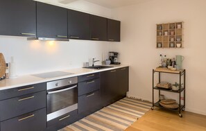 A modern kitchen with dark cabinets, a built-in oven, a coffee machine, and a small shelf with kitchenware. - Amazing apartment in Ebeltoft with house sea view (Ebeltoft)