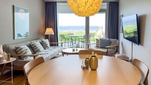 Un salon moderne avec une table ronde en bois, un canapé, un téléviseur et une vue sur l’extérieur.