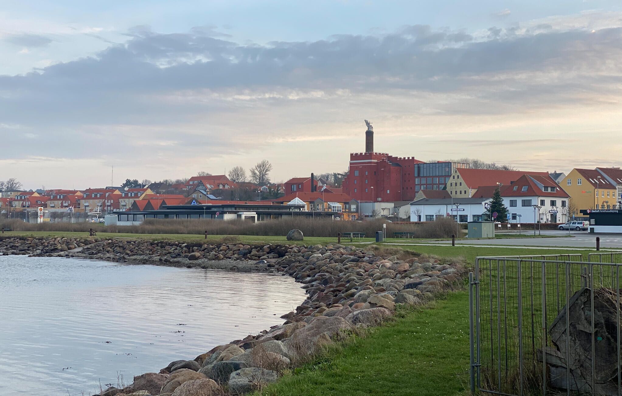 Rannikkokaupunki, jossa on huomiota her ättävä punainen rakennus, kivinen rantaviiva ja punakattoisia asuintaloja.