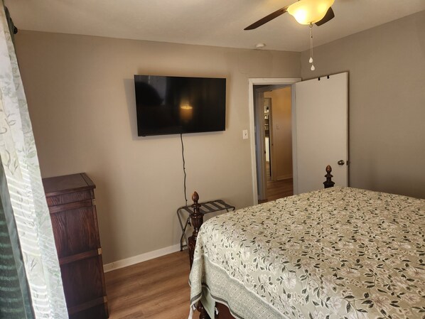 Un dormitorio con cama, cómoda, televisor montado en la pared y ventilador de techo.