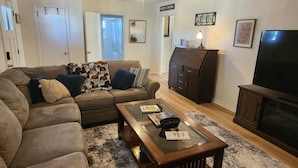 A living room with a sectional sofa, a glass coffee table, a dark wooden cabinet, a television, and a ceiling fan. - The Brenham Abode is pet friendly and conveniently located close to downtown. (Brenham)