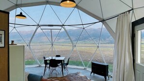 Quarto em cúpula geodésica com mesa e cadeiras de jantar, um sofá e vista do horizonte através de amplas janelas.
