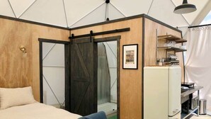 Quarto compacto com cama, uma kitchenette pequena e uma porta deslizante que dá para o banheiro.