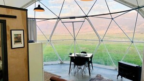 Quarto em formato de cúpula geodésica com mesa e cadeiras, um sofá e um lustre pendente.