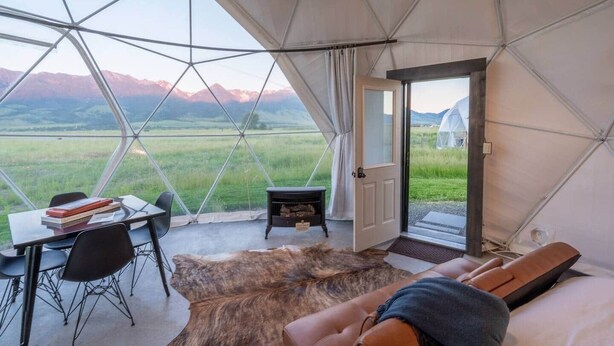 Alojamento em tenda com área de refeições, lareira e cama com vista para as montanhas.