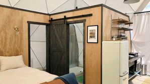 Une chambre comprenant un lit, une commode, un réfrigérateur et une porte coulissante donnant accès à un espace douche.