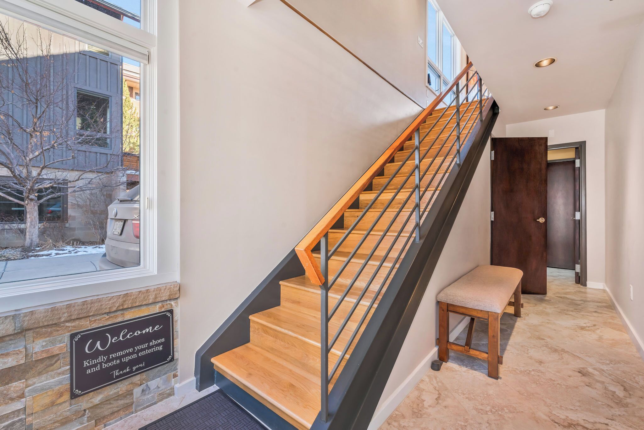 A modern staircase with wooden steps and metal railings, a welcome sign, and a bench at the bottom.