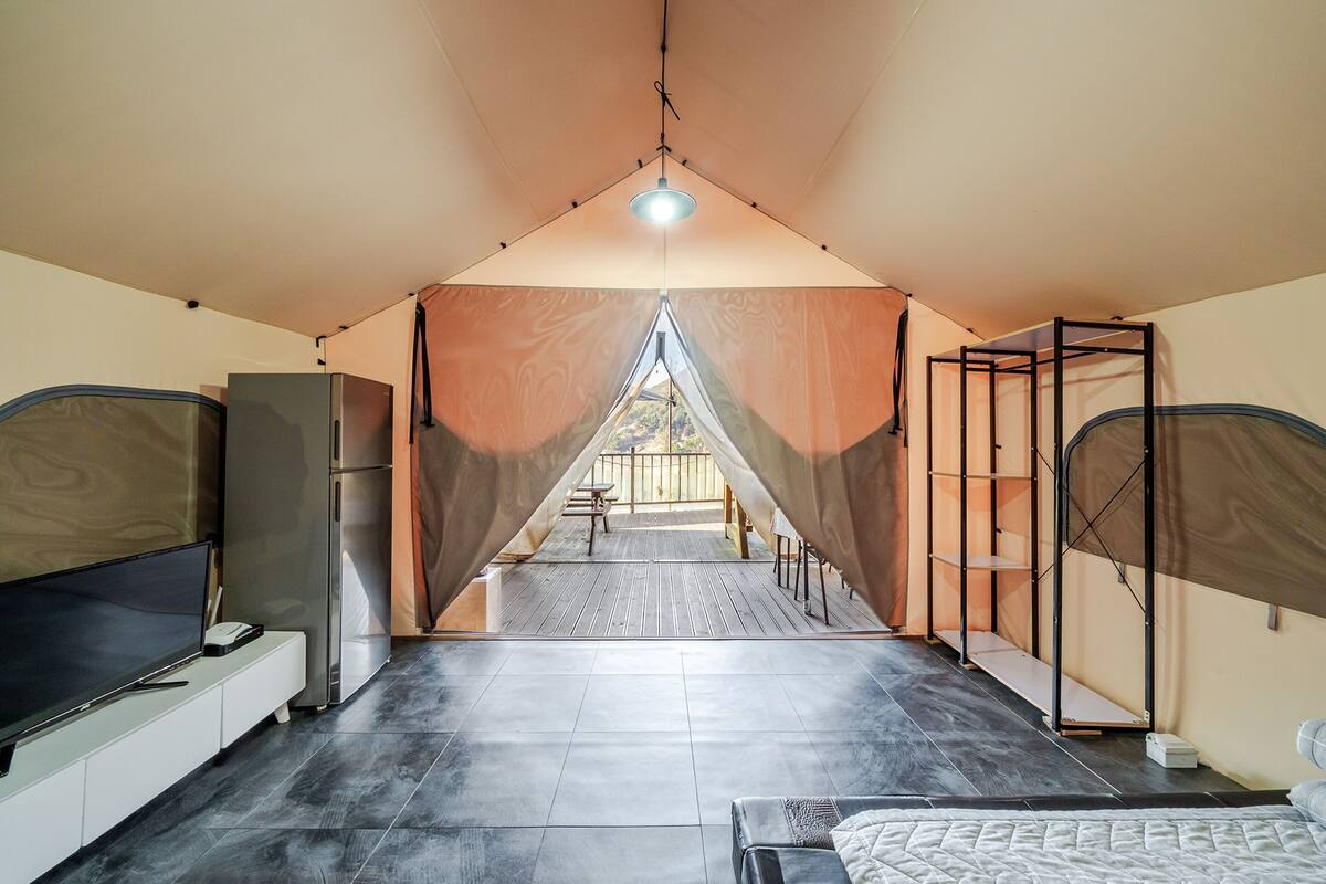 A tented accommodation with a kitchenette, a flat-screen TV, and a bed.