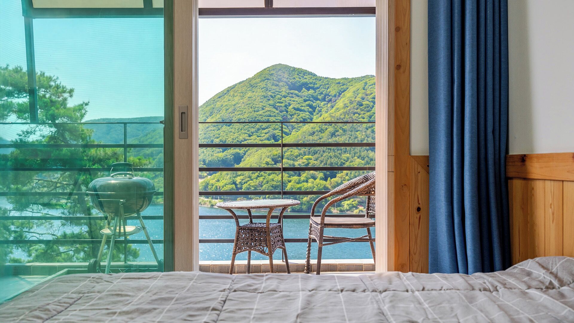 Un dormitorio con cama, un balcón con mesa y sillas, y vistas a una montaña y un lago.