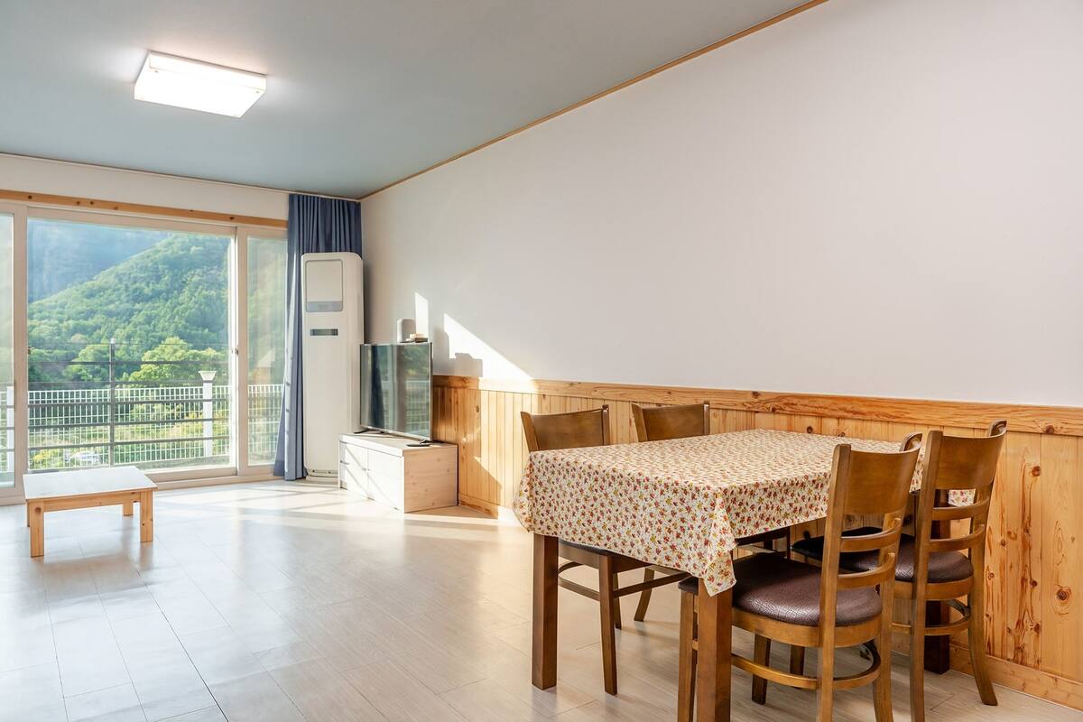A dining area with a wooden table and chairs, a bench, and a large window with a view of greenery.