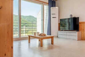 A room with a wooden table, a television, and a large window with a view of greenery. - Goseong Sand & Sea Glamping & Pension (Goseong)