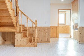 Una escalera de madera que sube a un segundo piso en una habitación con paredes y piso de tonos claros.