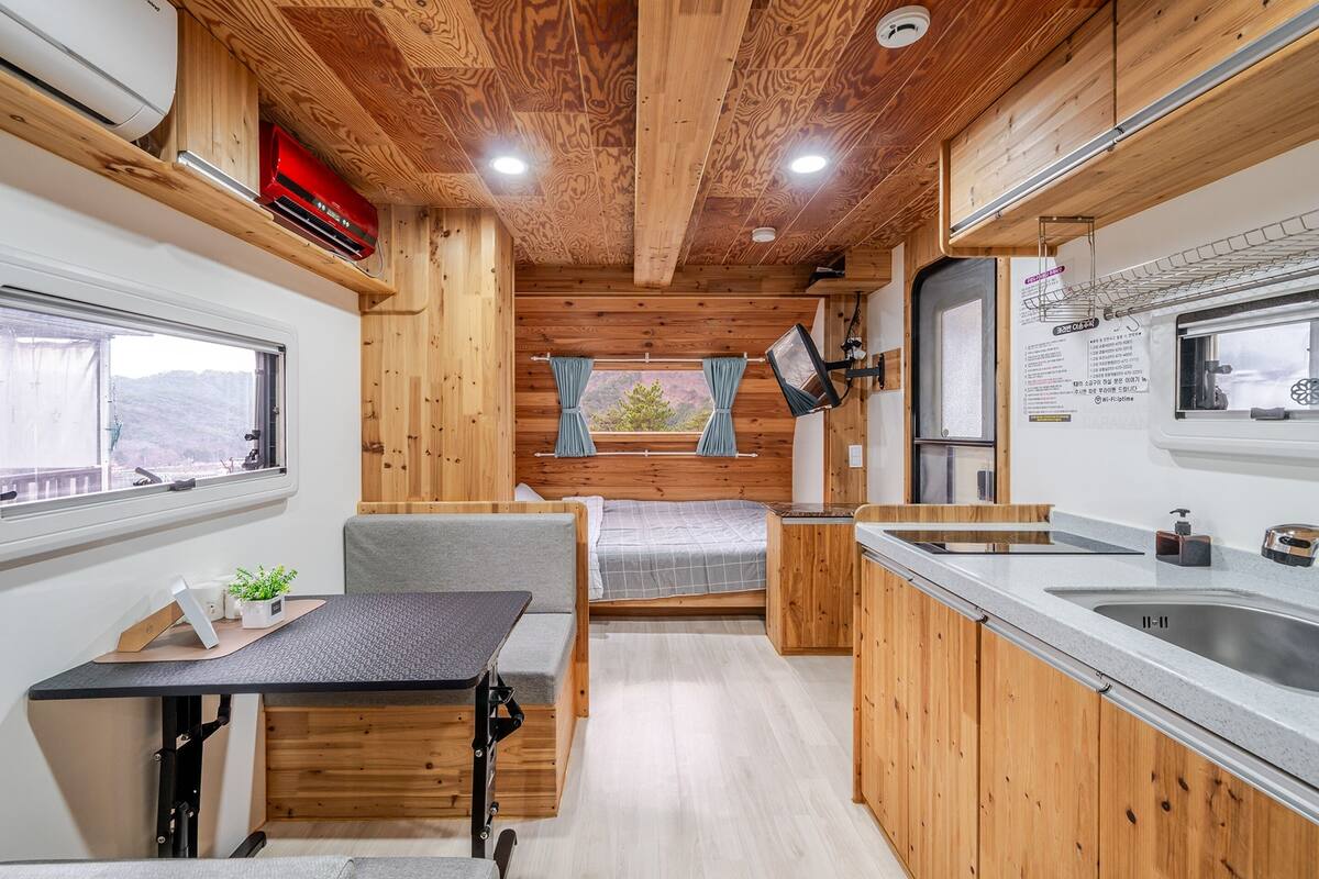 A compact RV interior with a kitchenette, a dining area, and a sleeping space.