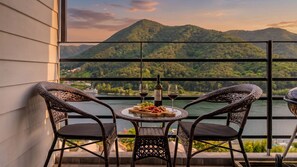 Un balcon avec des fauteuils en osier, une petite table ronde et une vue sur un lac et des montagnes.