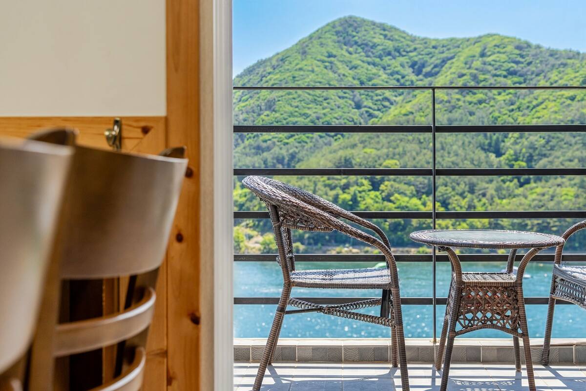 A balcony with wicker furniture overlooking a mountainous landscape and a body of water.