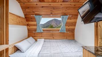 A bedroom with a wooden ceiling, a bed with a grey checkered duvet, and a window with curtains.