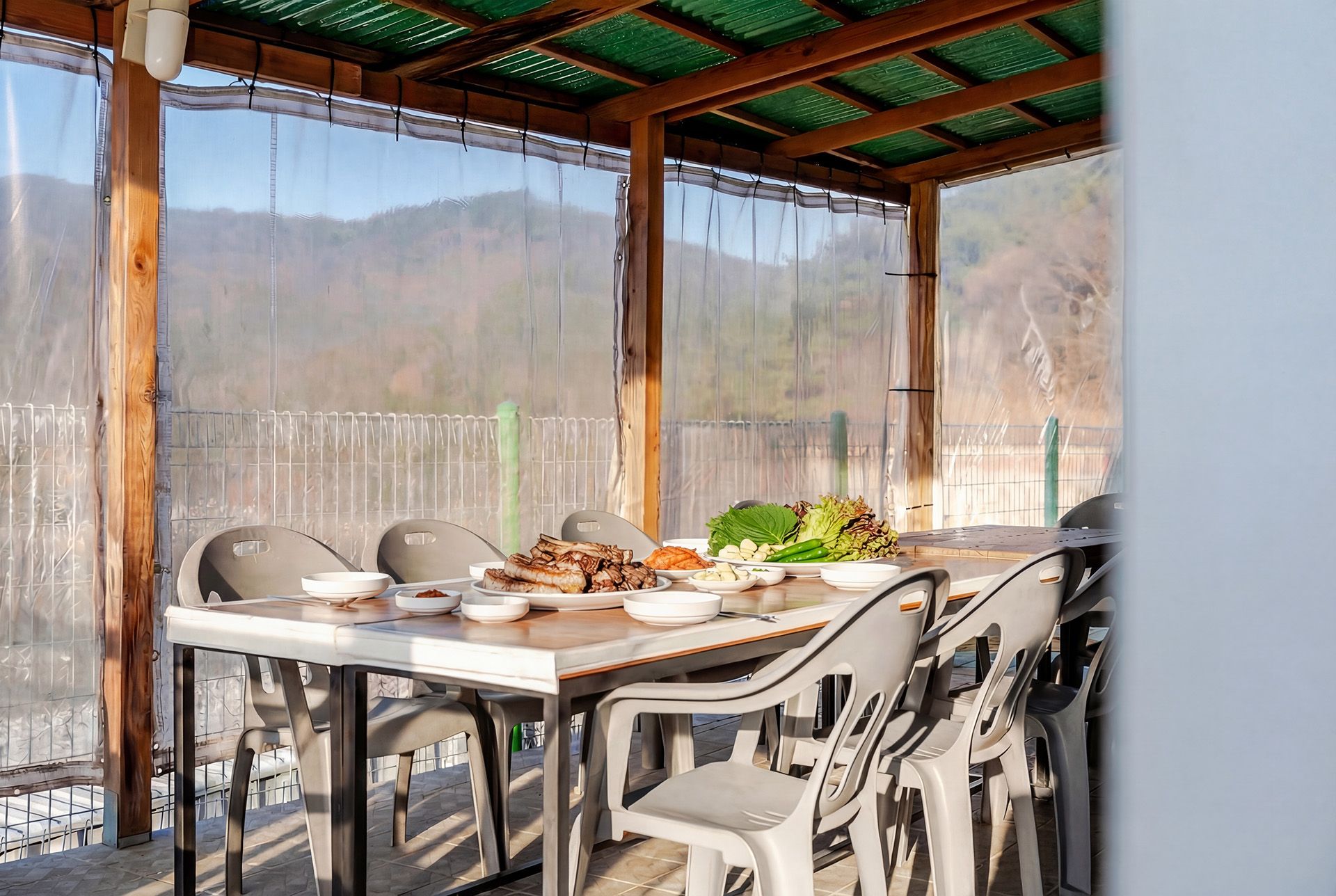 A covered outdoor dining area with a table set for two, surrounded by chairs.