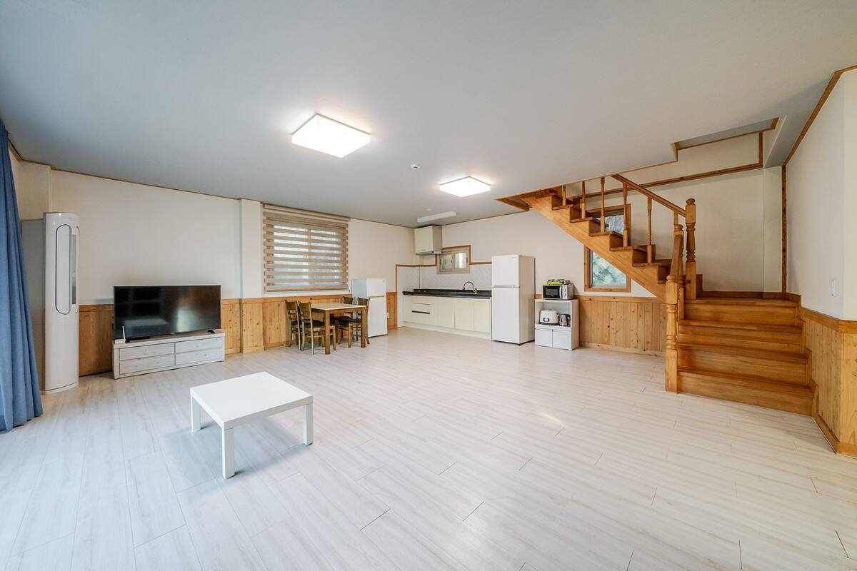 A spacious living area with a wooden staircase, a kitchen, and a dining area.