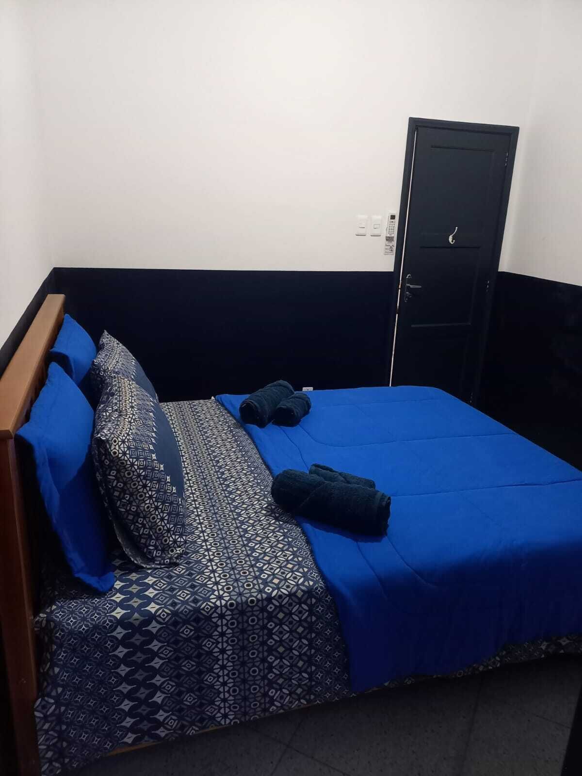 A single bed with a patterned bedspread and blue pillows, a black wardrobe, and a door with a handle.