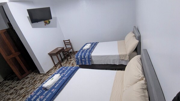 A small, clean room with two beds, a desk, a chair, and a TV on the wall.