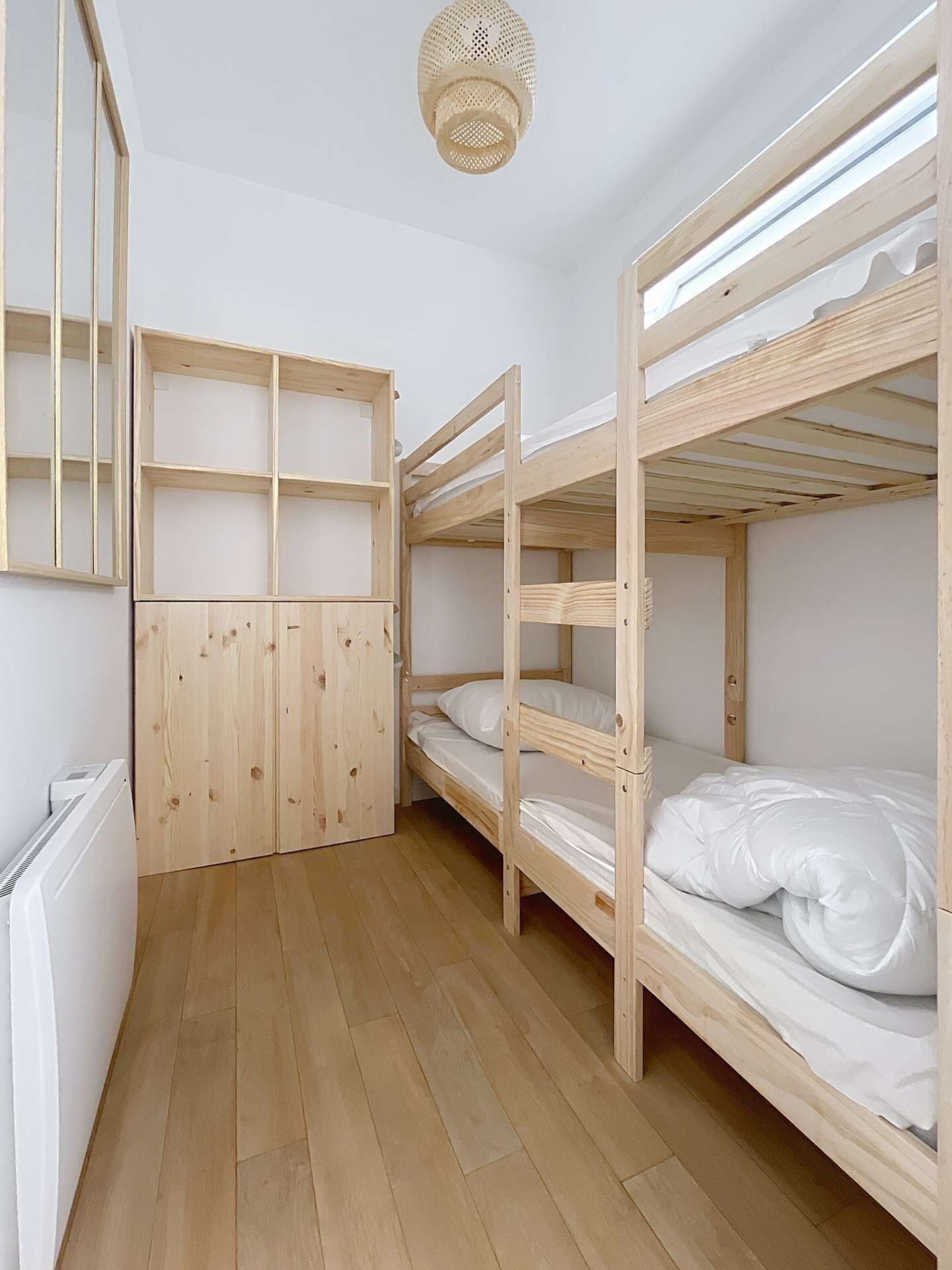 A bunk bed room with wooden walls and floors, a white radiator, and a woven ceiling light fixture.