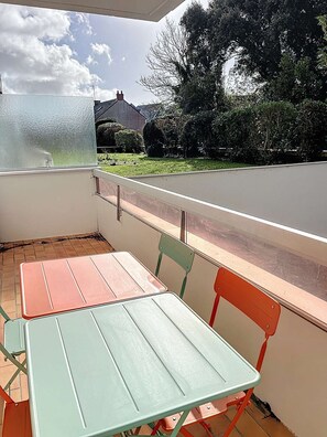 Un balcon avec une table et des chaises, donnant sur une maison et un jardin.