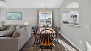 A dining area with a wooden table and chairs, a chandelier, and a view of the outdoors through a window. - Ironwood | Pool & Tennis Near the Beach (North Myrtle Beach)